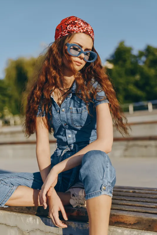 lifestyle woman in modern boho-western denim street style wearing blue sunglasses and red bandana, casual relaxed pose under natural sunlight with film color tones