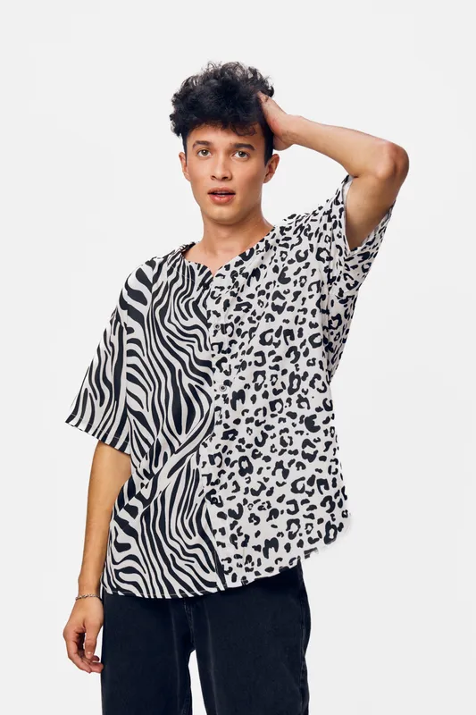 Young man wearing a stylish black and white animal print shirt, expressing surprise with hand on head and neutral white background, casual fashion pose.