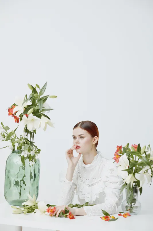 Elegant young woman in a white blouse posing with fresh flowers in soft pastel tones, evoking serenity and beauty, perfect for floral themed concepts