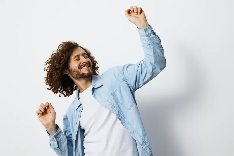 Happy young man dancing joyfully in a casual outfit against a light background, expressing positivity and carefree emotions, perfect for concepts of happiness and self expression