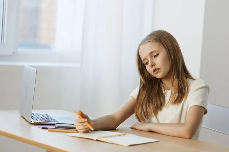 Thoughtful young girl writing in a notebook at a light filled study desk, showcasing creativity and focus with a minimalist aesthetic
