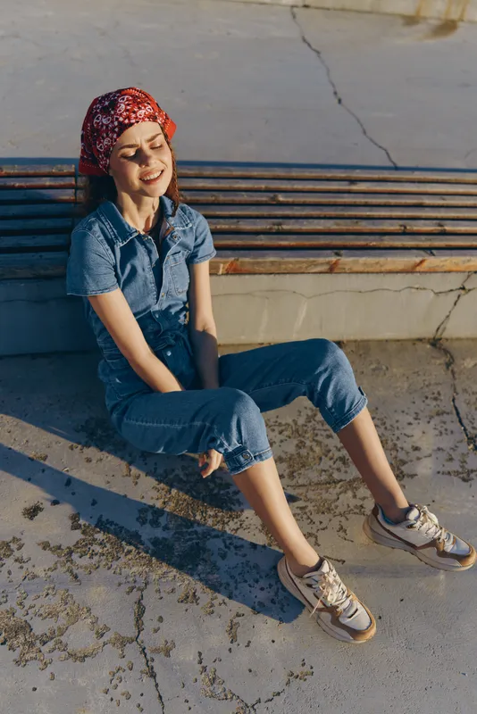 Lifestyle woman in modern boho-western denim street style with film color, relaxed and smiling outdoors in casual outfit and red bandana under bright sunlight.