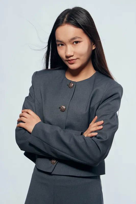 Young confident woman in formal gray business suit posing with crossed arms looking at camera in studio for professional portrait and corporate fashion concept.