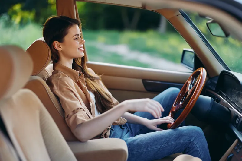 Young woman driving a vintage car, embodying freedom and adventure with a joyful expression, set against a natural green background, perfect for travel themes.