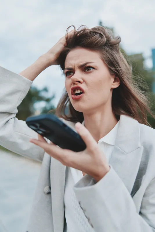 Angry businesswoman on a phone call expressing frustration with a serious expression in a stylish suit outdoors.