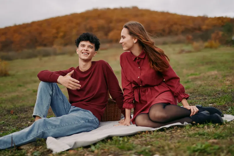 An intimate outdoor scene features a young couple on a blanket in a golden autumn field, sharing smiles and warm conversation, radiating authenticity and believability.