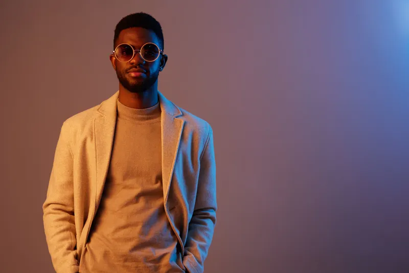 Stylish man wearing sunglasses and a neutral outfit, exuding confidence against a colorful gradient background Modern fashion concept with urban vibes