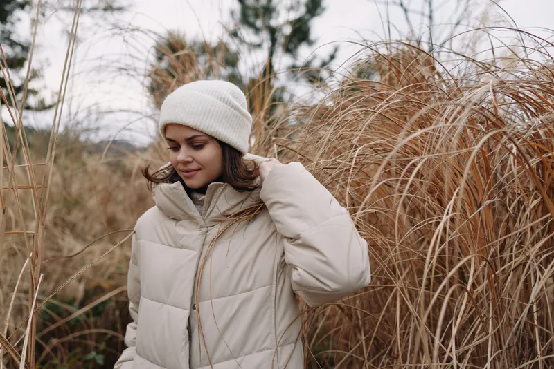 Woman wearing a beige winter coat in an outdoor portrait among tall grasses, soft light and calm mood in a natural setting on a windy day