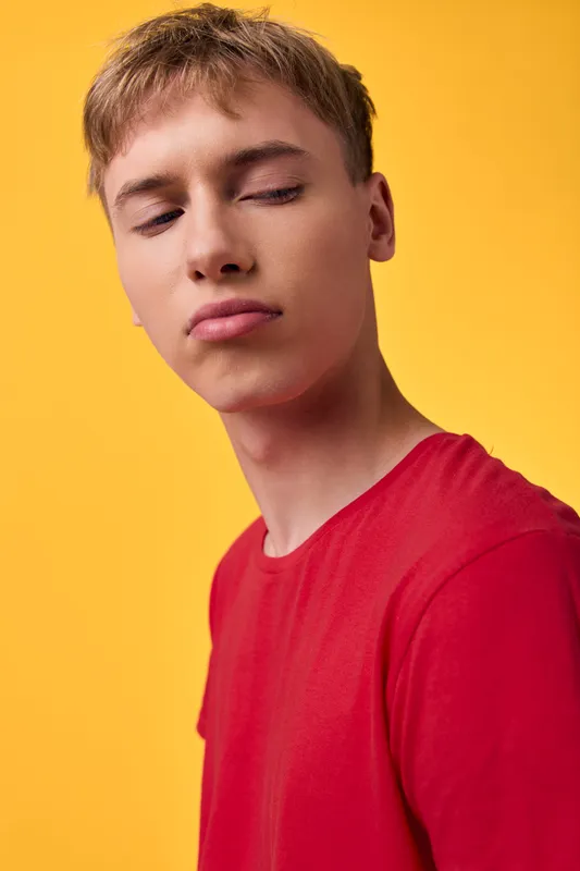 Youthful male in a red shirt against a bright yellow backdrop, calm expression, studio shot with soft lighting, clean composition and close up angle, minimal background and modern fashion vibe