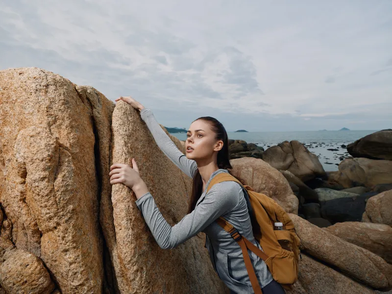 Young woman exploring rocky landscape, wearing sporty outfit and backpack, exuding determination in nature setting with ocean view