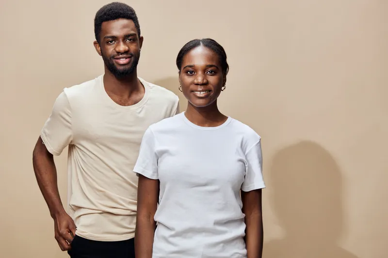 Smiling young Black couple wearing casual clothes against a beige background, representing love and togetherness in a warm and inviting atmosphere