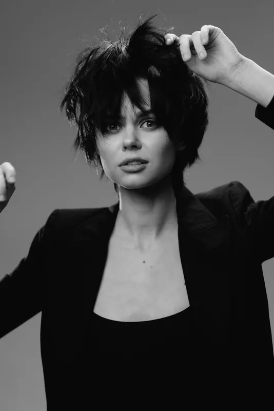 Black and white portrait of confident woman with tousled hair wearing dark jacket, expressive and stylish, minimalistic studio background