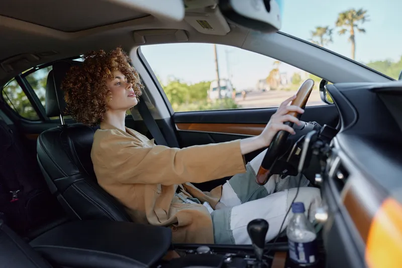 Confident woman driving a car, interior in focus, sunlit cabin, retro film color palette, casual outfit, relaxed road trip mood captured outdoors
