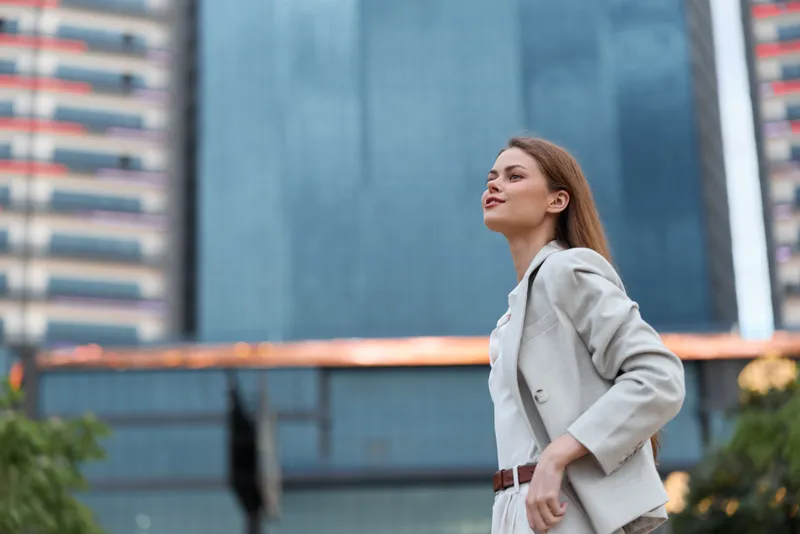 Confident woman in business attire standing against an urban backdrop, exuding professionalism and ambition with a stylish outfit and inspiring demeanor.