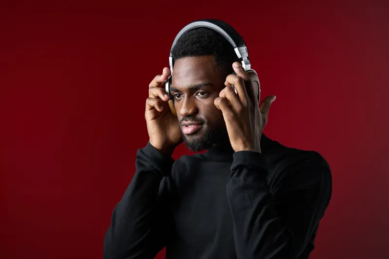 Young African man enjoying music with headphones on a red background, showcasing modern style and emotional connection to sound Perfect for music related concepts