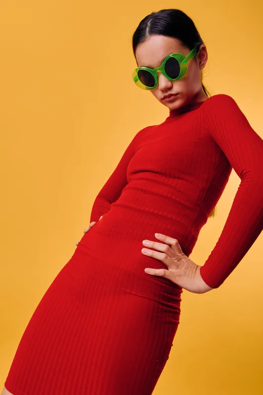 Woman in red dress and green sunglasses posing against yellow background fashion style and confident look with bright colors and modern outfit in studio.