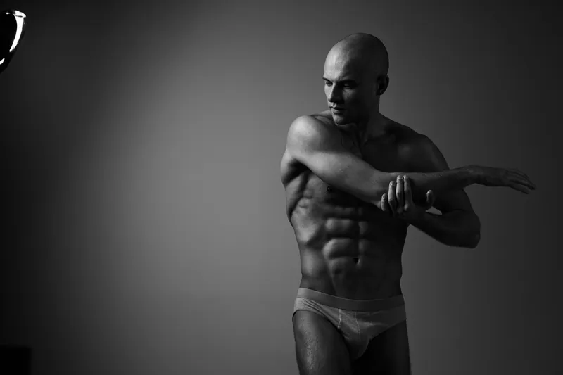 A muscular man stretching in a black and white setting, showcasing strength and fitness. The image highlights dedication and a focused expression that inspires.