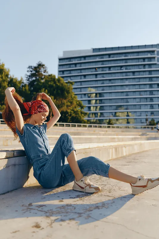 Lifestyle woman in modern boho-western denim street style relaxing outdoors with bright film color, casual outfit, and sunny urban background atmosphere.
