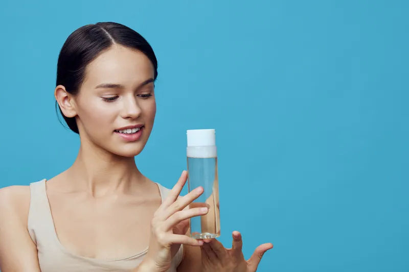 Young woman admiring a skincare product against a blue background, showcasing beauty and self care with a serene expression, perfect for wellness promotions