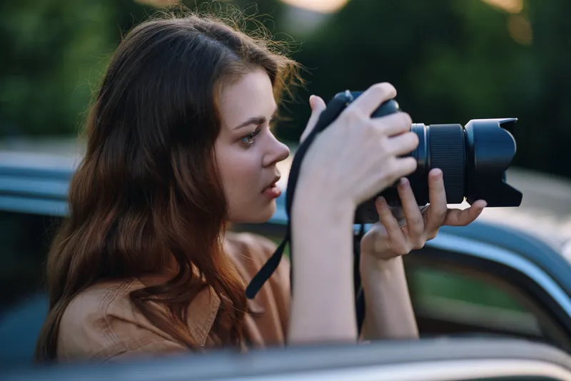 Female photographer capturing moments outdoors with a professional camera, showcasing focus and passion for photography, surrounded by lush greenery.