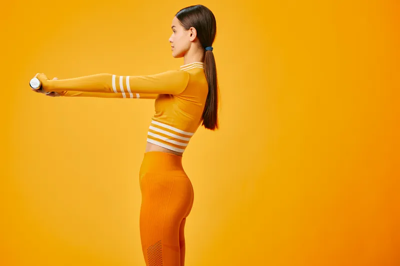 Woman athlete in bright fitness outfit extends a baton against a bold orange backdrop, showcasing sport, training, energy and motion in a dynamic studio shot.
