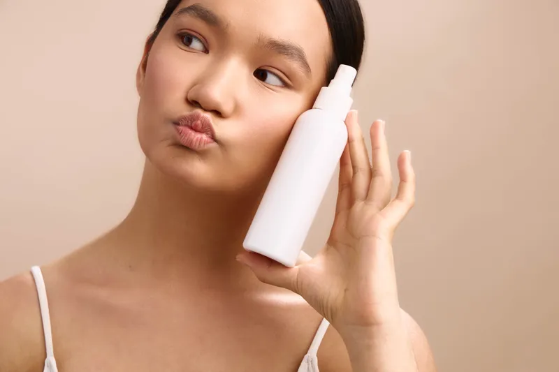 asian woman applies skincare product and smiles softly in a sleek bathroom setting. a calm, confident mood conveys self care and beauty routine, emphasizing asian woman in everyday wellness scene.