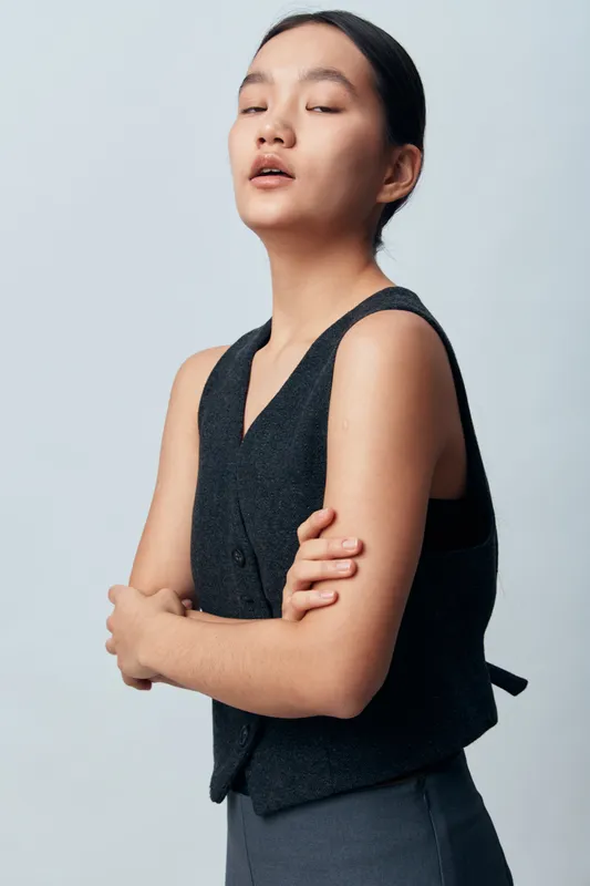 Young woman in sleeveless black vest standing with crossed arms against light background. Portrait of confident female model with natural makeup and neat hairstyle for fashion or beauty.