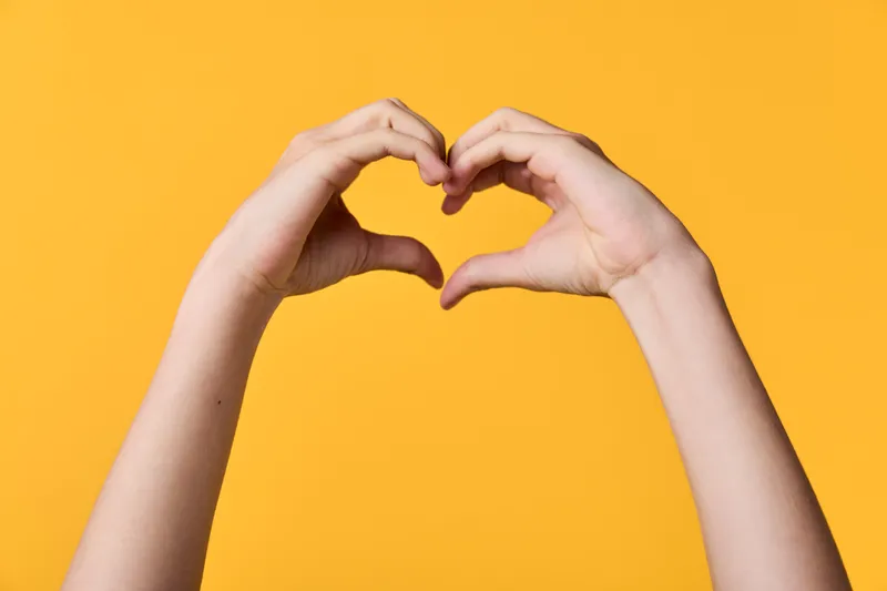 Hands forming a heart gesture against a bright yellow background, symbolizing love, care, and unity in a simple, expressive frame for warm messaging and positive vibes in creative stock imagery.