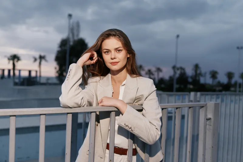 confident woman in beige business suit posing outdoors with urban background at dusk, professional young woman with calm expression