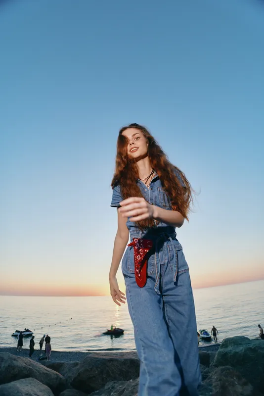lifestyle woman in modern boho-western denim street style enjoying outdoor sunset by the sea with film color effect and relaxed confident mood