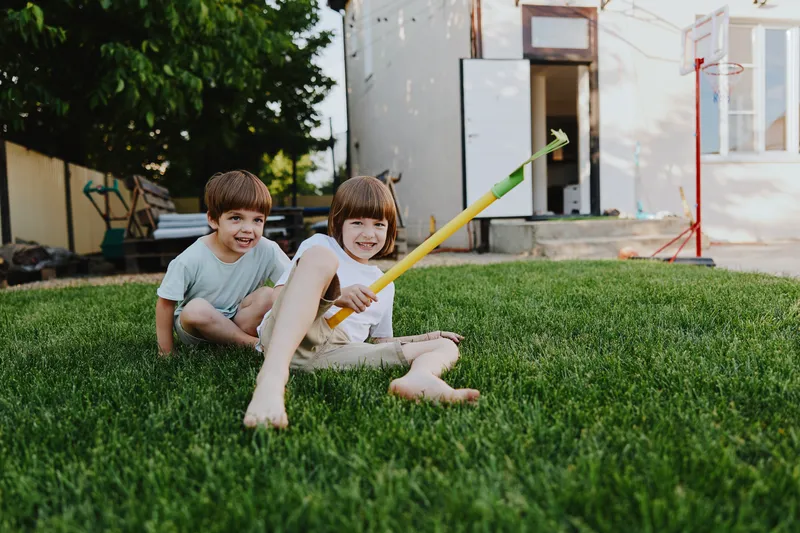 Two cheerful children enjoying a sunny day in the backyard, laughing and playing with a colorful water toy on the green grass, capturing the joy of childhood.