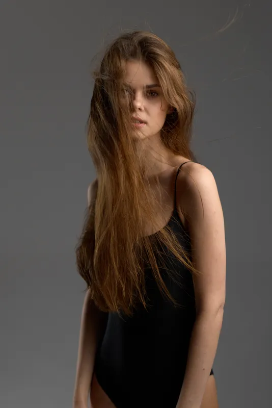 young woman with long hair wearing black sleeveless dress against gray background