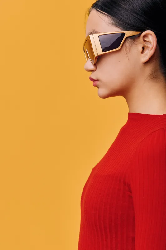 Woman with sunglasses in profile wearing red sweater on bright orange background. Fashion portrait of stylish young female model with modern accessories and simple clean look.