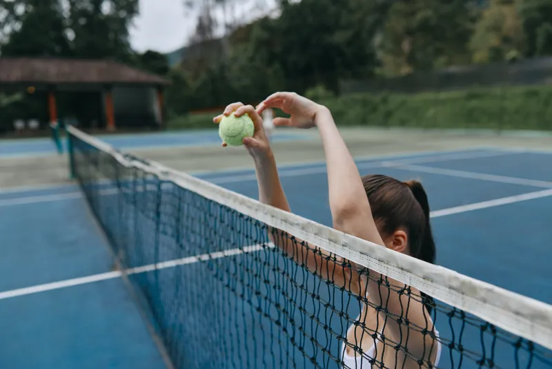 Female tennis player preparing to serve with a tennis ball, showcasing athleticism, focus, and outdoor sports in a vibrant blue court setting