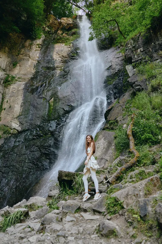 woman hiking near waterfall, natural scenery, rocky terrain, green forest, outdoor adventure, active lifestyle, fresh air, nature exploration.
