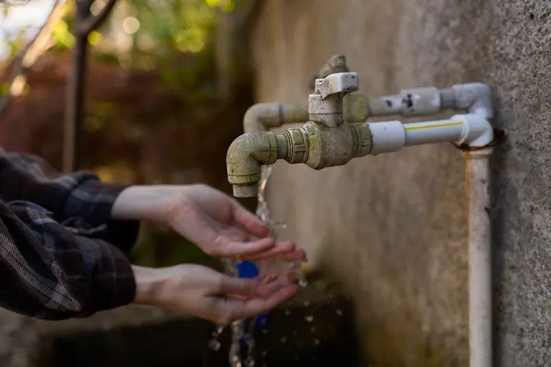 A close up of hands under a dripping faucet outdoors, washing with clear water. The scene conveys everyday hygiene, calm self care, and simple routine