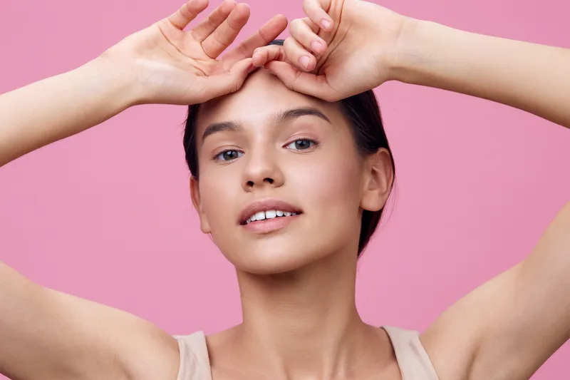 Young woman with clear skin and an elegant pose against a soft pink background, showcasing beauty and confidence in a minimalist style