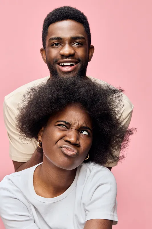 Two young African individuals expressing joy and playful emotion against a pink background, showcasing vibrant personalities and carefree spirit in casual clothing