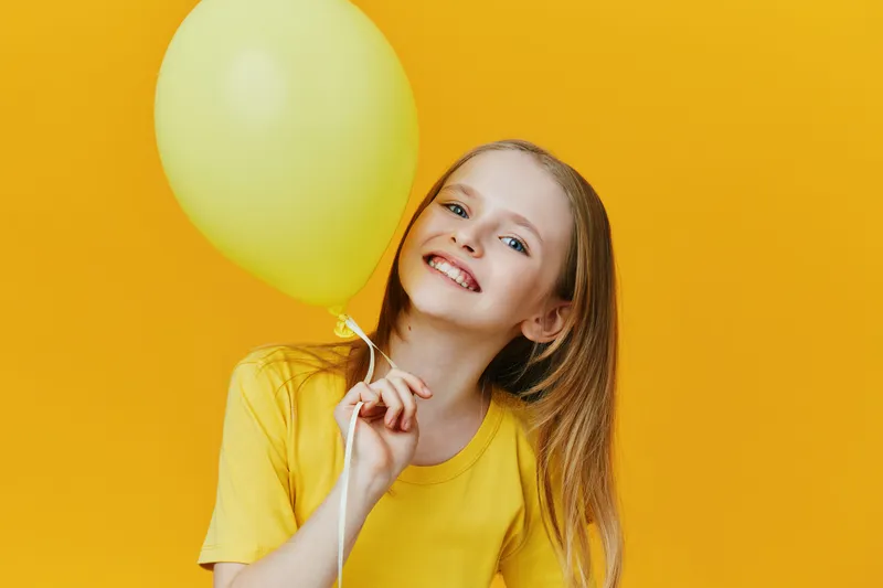 Happy girl with a yellow balloon against a bright yellow background, wearing a cheerful yellow shirt, expressing joy and positivity