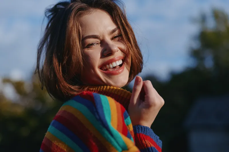 Smiling woman portrait in a colorful sweater outdoors in sunlight, happy and joyful closeup showing natural beauty, laughter and casual knitwear style in daytime.