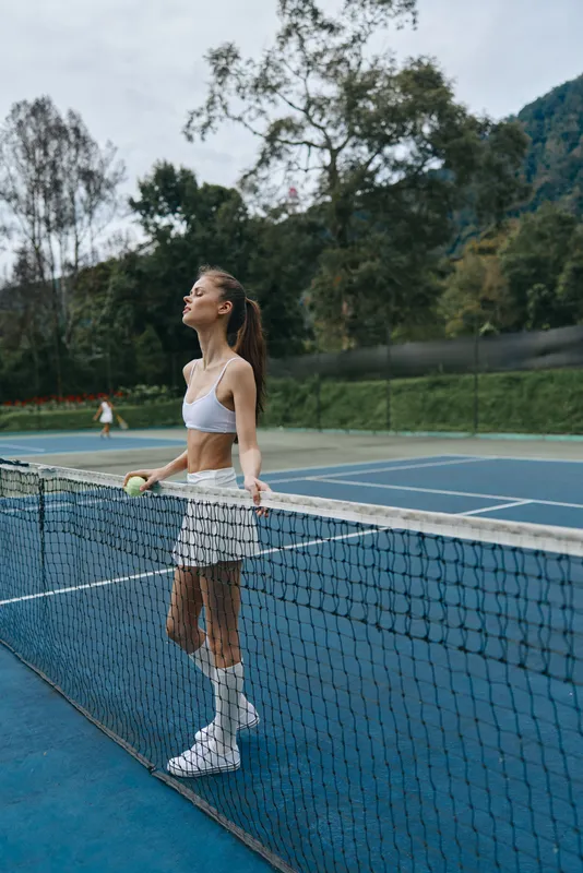 Young female tennis player practicing on outdoor court, showcasing concentration and athleticism with a fresh summer vibe and natural green background