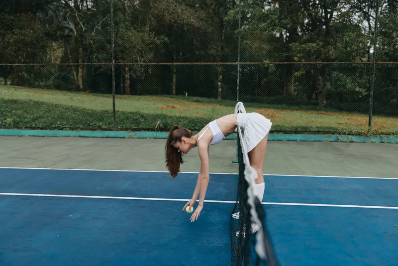 Female tennis player stretching before a match on a blue court, wearing a sporty outfit, conveying determination and focus in a natural outdoor setting