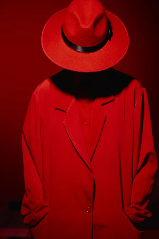 Fashion model wearing an oversized red coat and matching wide-brimmed hat poses against a red backdrop. Concept for beauty, creative style, fashion editorial.