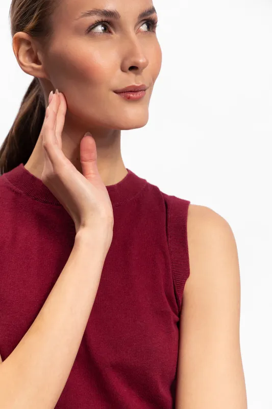 Portrait of a young woman in a burgundy sleeveless top looking thoughtfully to the side with hand near face against a white background. Concept for beauty and contemplation.