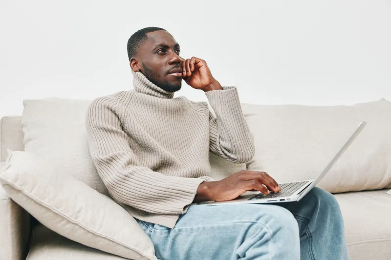 Stylish young African man in a cozy sweater working on a laptop at home, promoting the modern remote work lifestyle and comfort at home