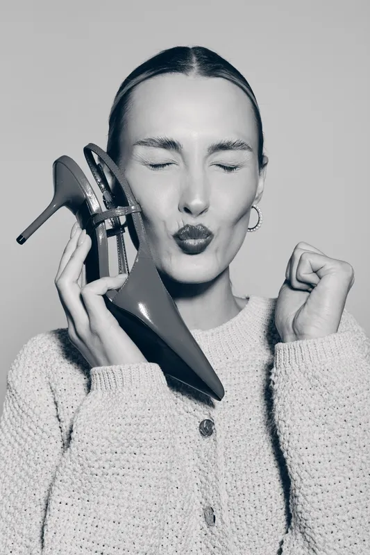 Blonde white woman with fair skin holding high heel shoe near face, eyes closed and lips puckered. Concept for fashion, style, and happiness.