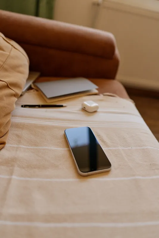 Casual indoor scene with a smartphone resting on a striped bed cover, warm natural light, cozy home atmosphere, everyday life focused on technology.