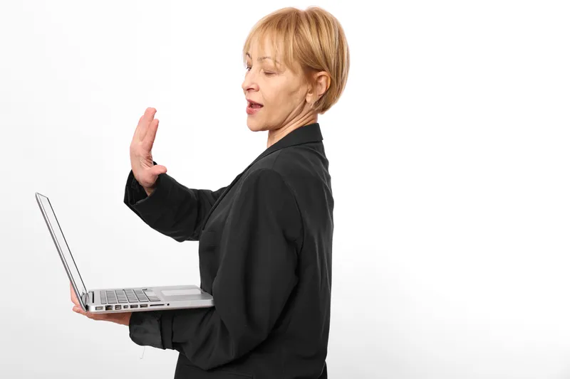 Business woman with blonde hair holds a laptop in profile view, raises hand gesture while communicating, isolated on white studio background, technology