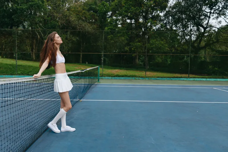 Athletic model in a white tennis outfit exuding confidence on a sunny court, showcasing the spirit of sports and healthy lifestyle