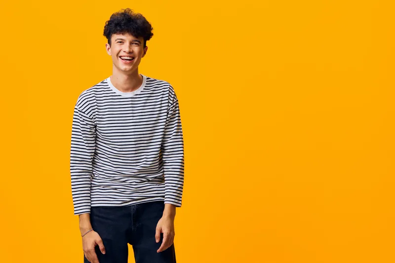 smiling young man in striped shirt standing against vivid orange background, casual style, joyful expression, curly hair, studio portrait with bright colors